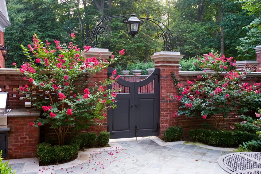 An example of a beautiful brick fence with landscaping and wrought iron elements