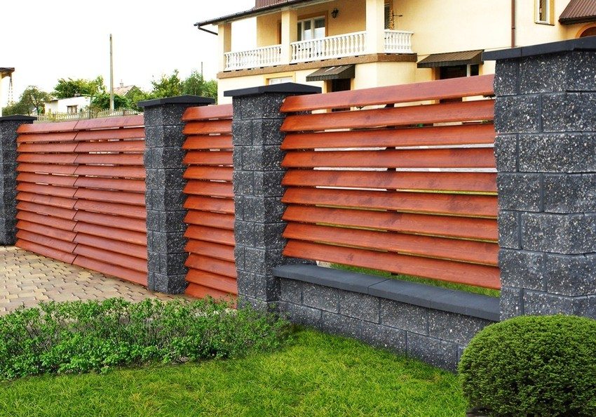 Combined fence made of wood and stone. The boards are arranged in a herringbone