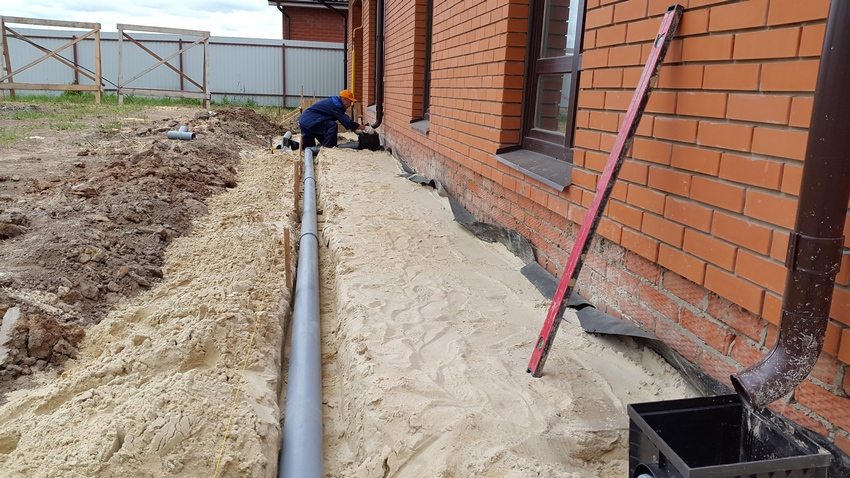 The process of creating a sand and crushed stone pillow. Step 1: sprinkle sand with a layer of 10 cm with pouring and tamping, along the wall of the house put roofing material with a height from the base of the trench to the supposed top of the blind area (expansion joint)